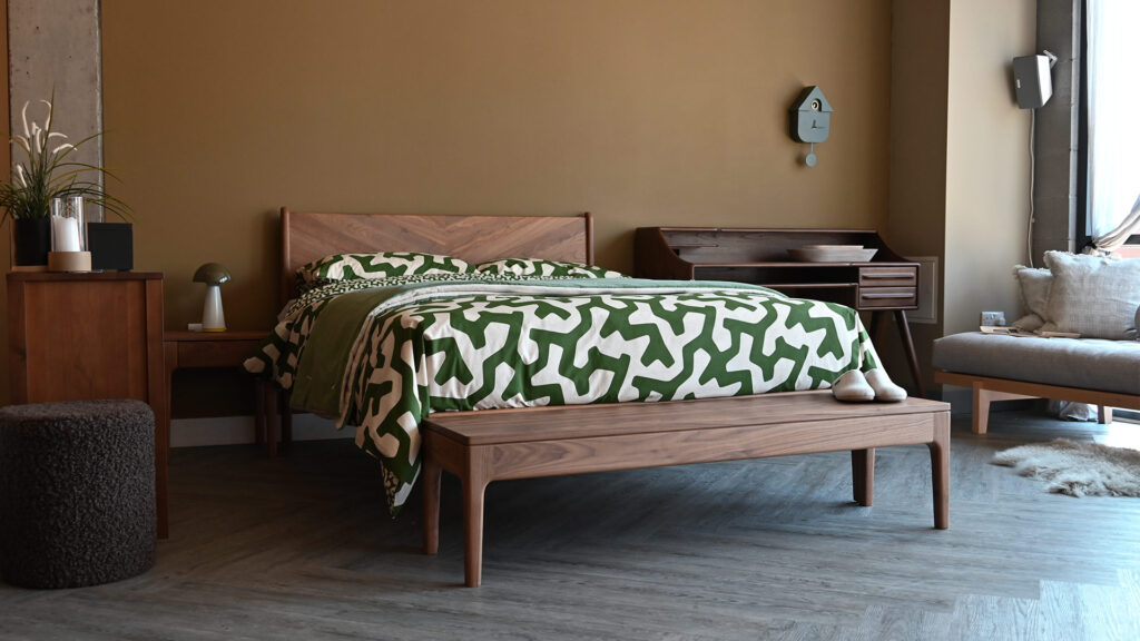 Green and white abstract bedding on solid walnut bed frame. Walnut bench and teak desk also in shot.