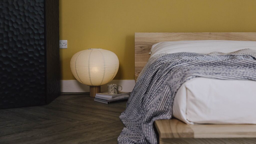 Ash Oregon bed frame with white linen and a blue striped bedspread. Japanese inspired large paper lamb to the side.