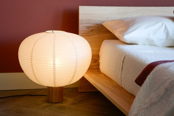 Balloon Shade Lamp sat on floor next to low Oregon bed base with red and white bedding.