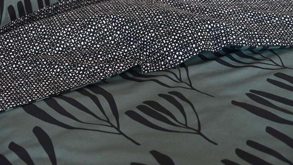 Close up of green bedding with black frond print. Black patterned reverse also visible.