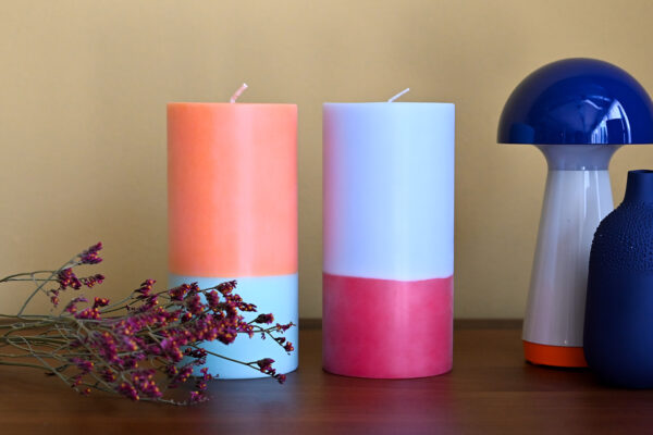 2 large colour block candles.One aqua and orange the other cornflower blue and pink. Flowers, a blue vase and a mushroom lamp also in image.
