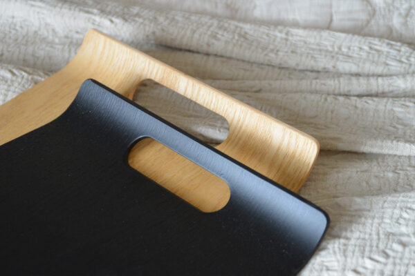 2 curved trays, one black, one oak, laid on a white textured bedspread.