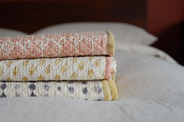 Stack of three contrast edged boho throws, one with ink blot pattern, one mustard diamonds and one terracotta tiles.