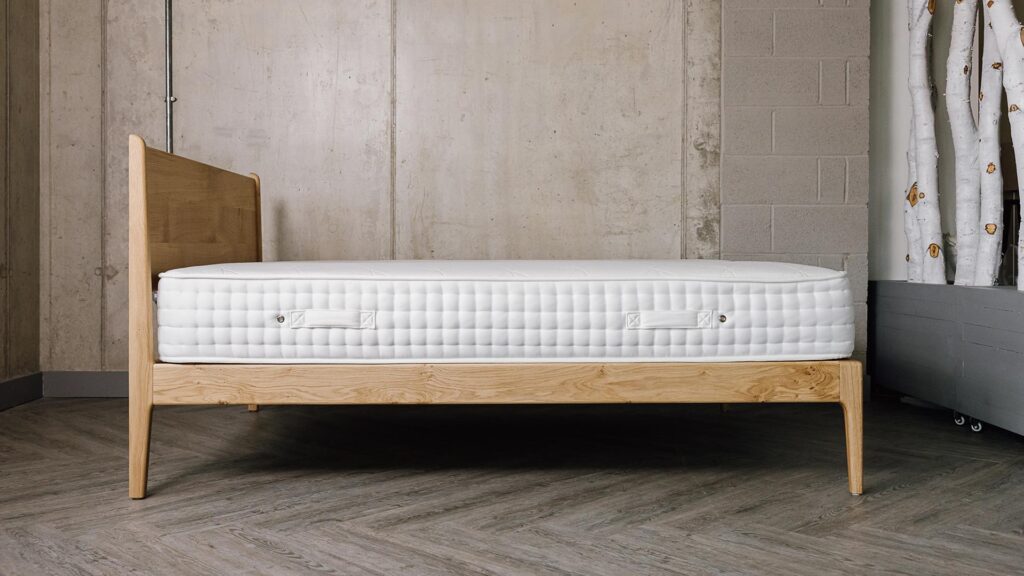 side view of English oak Camden bed with mattress. Knots and grain pattern visible on the side rail.