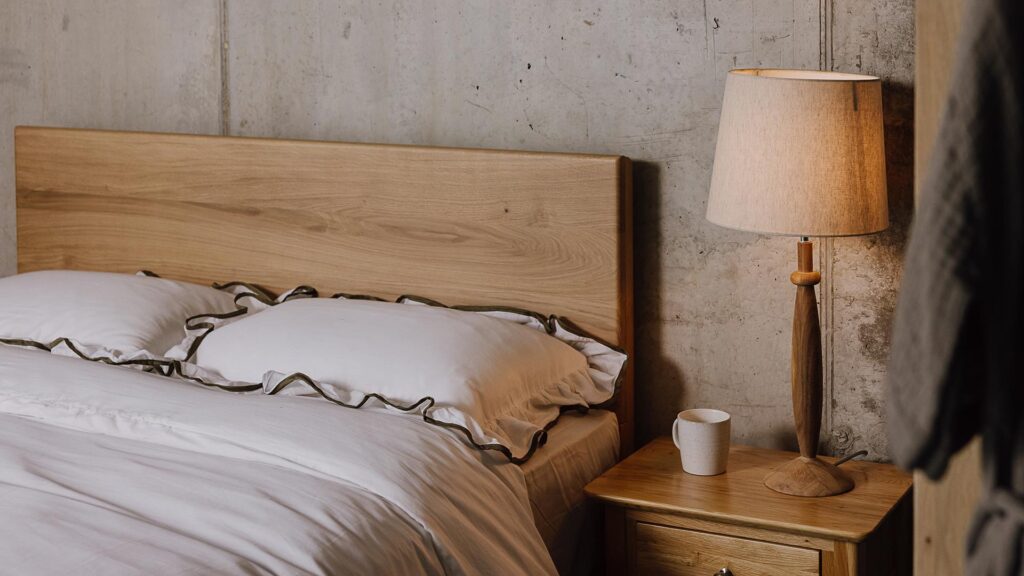 A close up angled image of the English oak Chiswick. The image focuses on the headboard panel. The bed is dressed in the white bedding with green ruffled border.