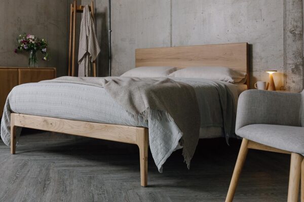A low angled shot of the English oak Chiswick. The bed is dressed in the organic linen ecru bedding, a silver grey embroidered bedspread and a beige pure wool throw.