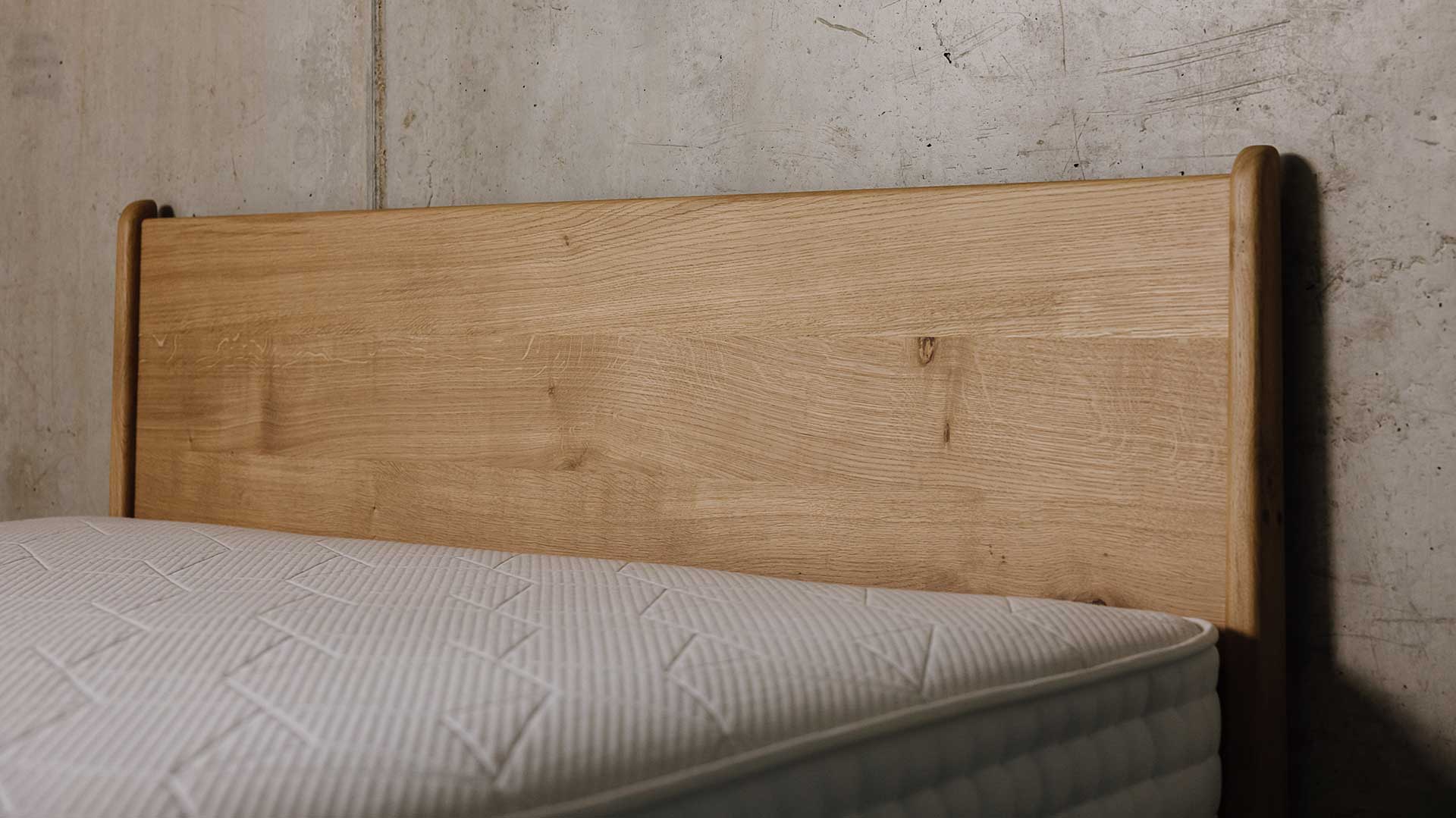 Headboard of Camden bed in English Oak. Some knots and swirls of grain pattern visible in the timber.