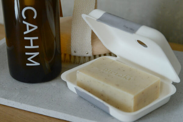 Meraki sesame scrub soap in white tray. Other bathroom accessories in the background.