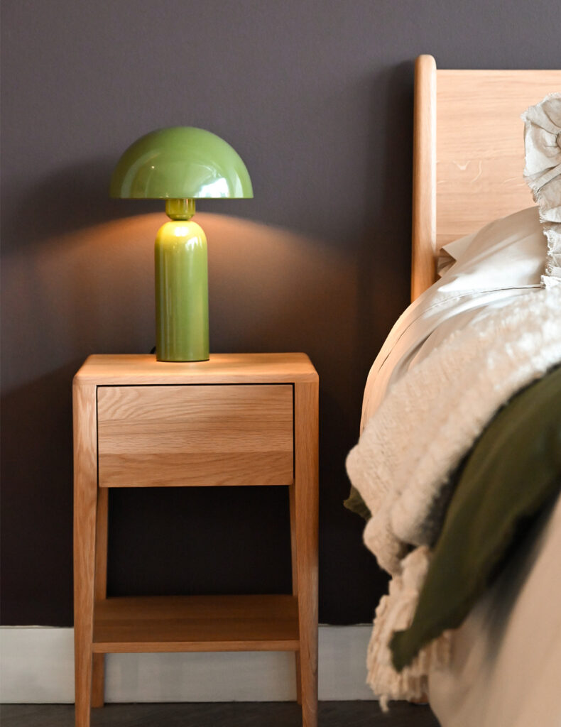 Image showing a tall retro style lamp with an enamel finish in a mid-green colour. The lamp sits atop a bedside table, and next to the Camden handmade bed base.