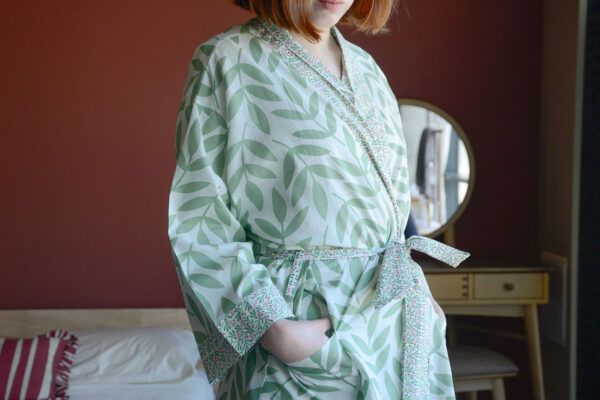 Model facing side wearing pale green frond pattern kimono with pink detailing to the sleeves, lapels and tie.