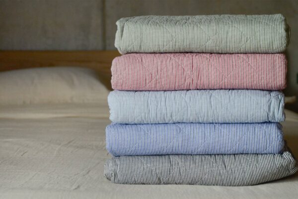 stack of five folded quilted striped throws. Green, red, pale blue, dark blue and dark grey.