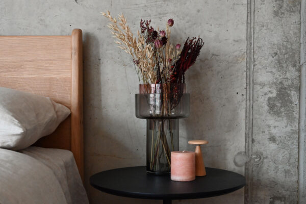 Two tone glass vase with removable top section and wide opening. Large bouquet of flowers. On a black round table with a small lamp and candle.
