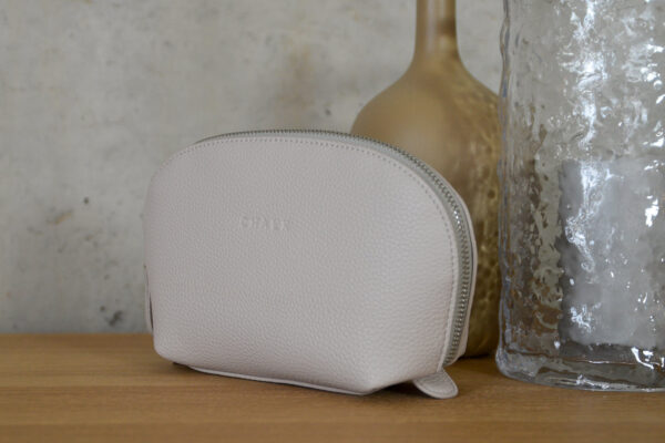 pale stone zip up makeup bag stood with 2 glass vases.