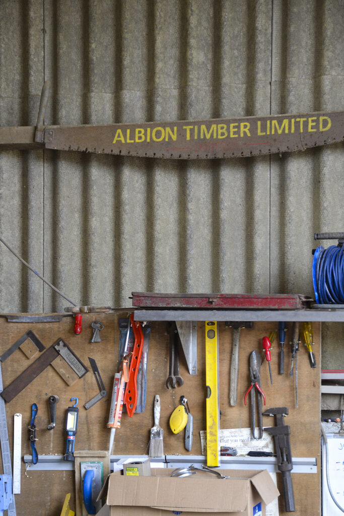 Image showing a decorative, old fashioned saw blade painted with the words 'Albion Timber Sheffield' on it. The saw blade hangs on a wall above a workbench, which holds many tools such as smaller saws, spirit levels and pliers.