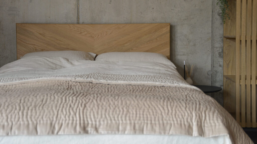oak bed frame with ecru linen and a quilted velvet almond throw.