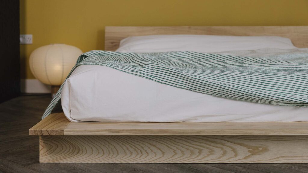 Green Striped bedspread draped over white bed linen on a ash platform bed frame.