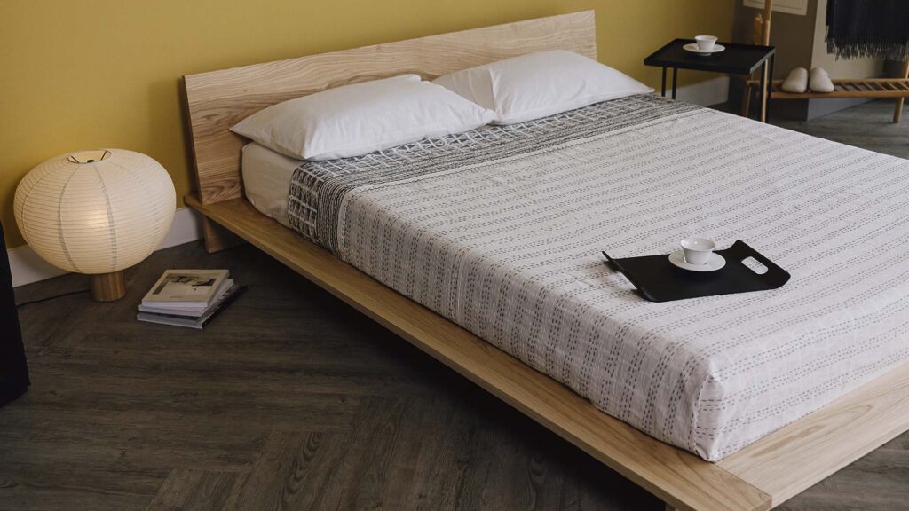 Ash platform bed base with striped bedspread.