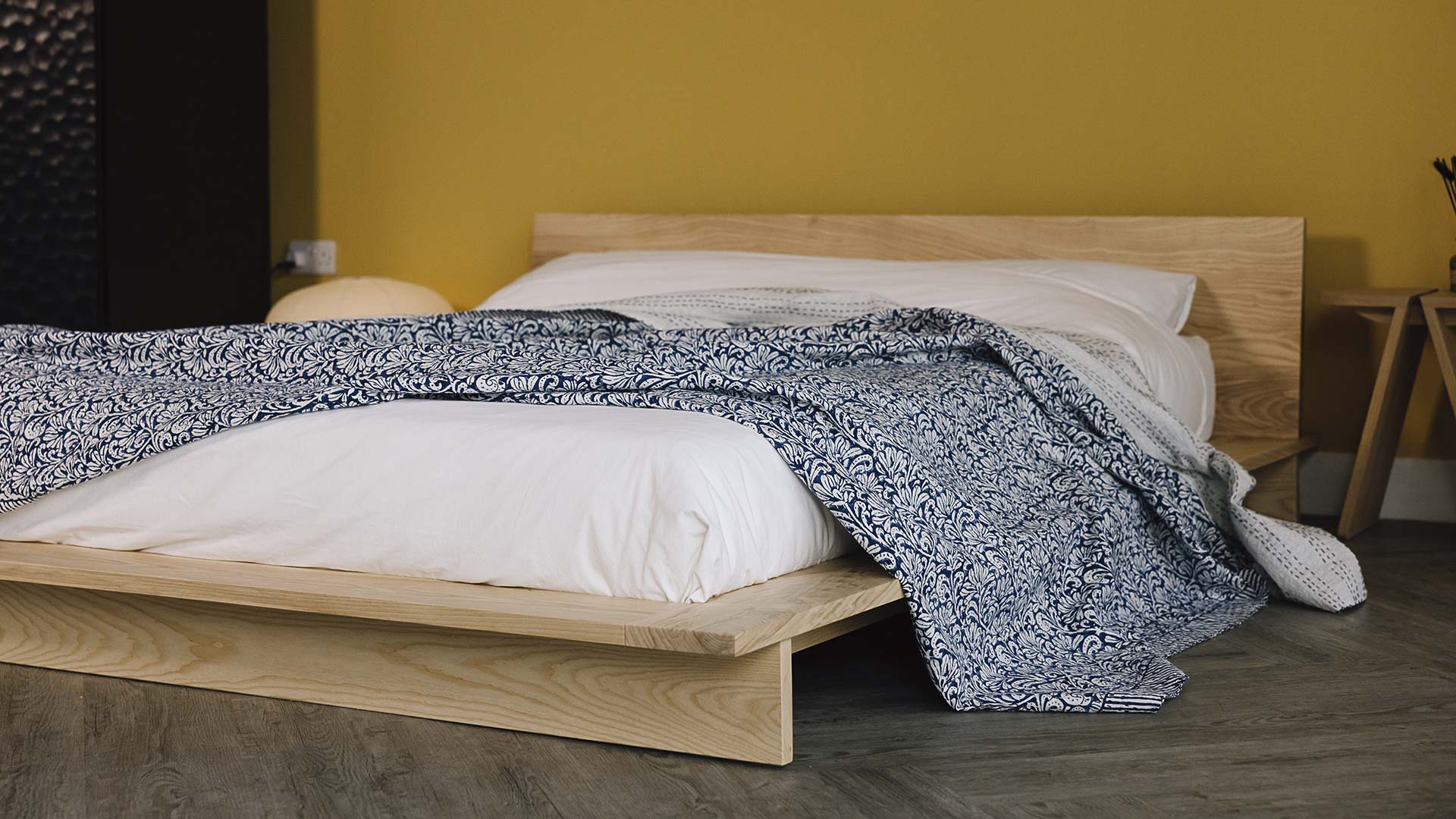ash bed frame with white linen, a floral blue bedspread on top.