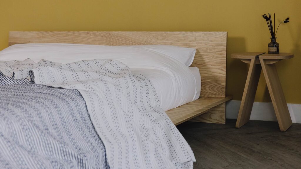 Blue stripe bedspread on an ash platform bed. Bed side table with diffuser to the side.