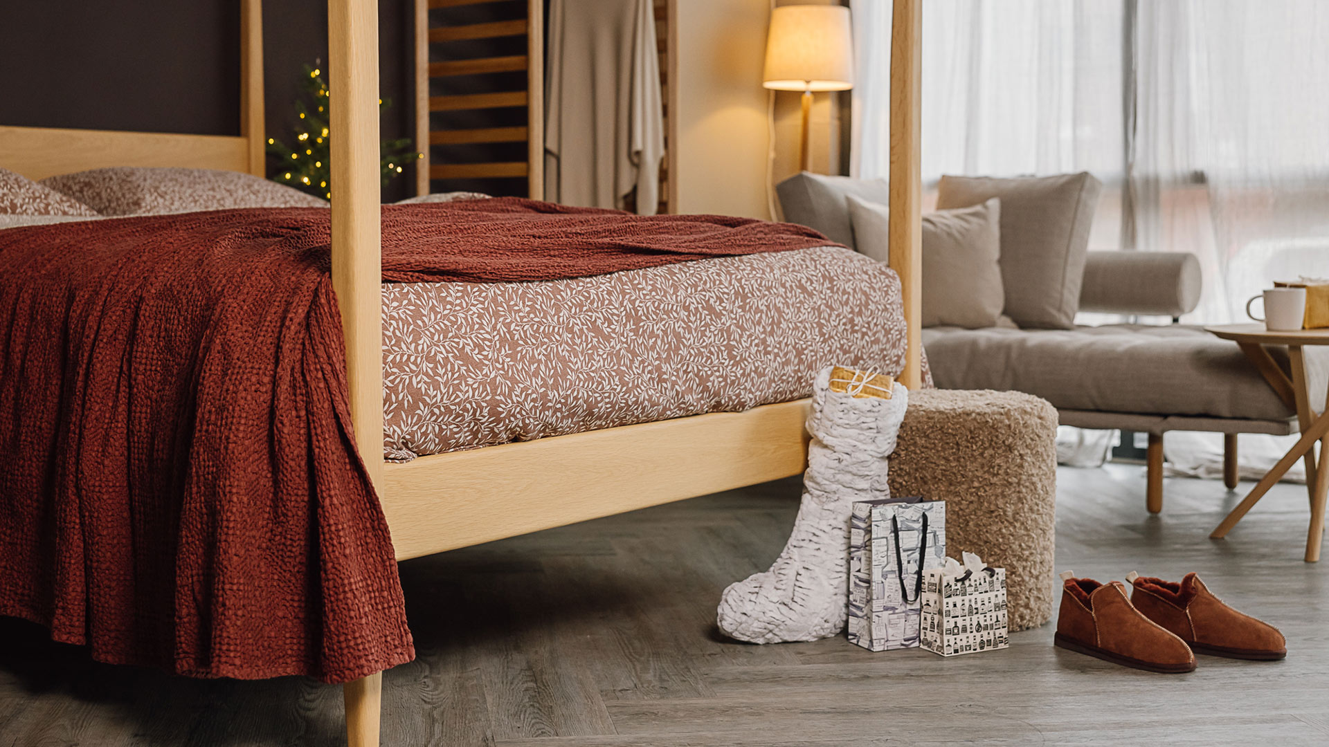 four poster bed with floral bed linen and red bedspread. Christmas stocking and gifts with slippers at the foot of the bed.