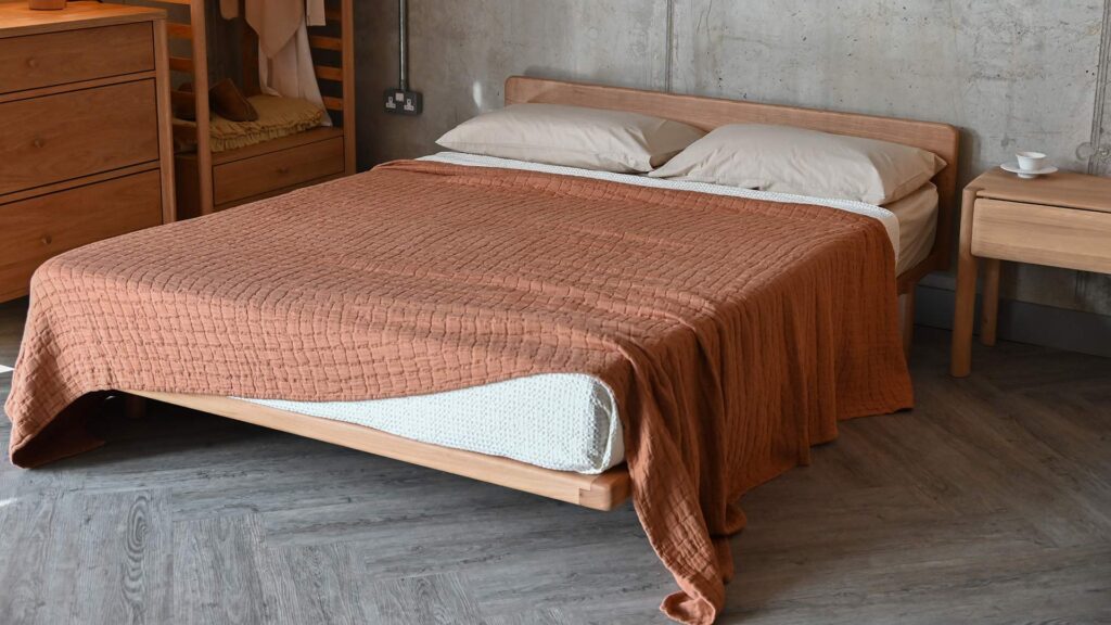 A terracotta textured cotton bedspread featuring a square pattern, displayed on a solid cherry Osaka bed base.