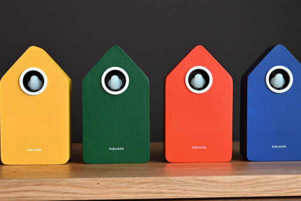 four alarm clocks with woodgrain pattern and white bird. One each in yellow, green, orange and blue.