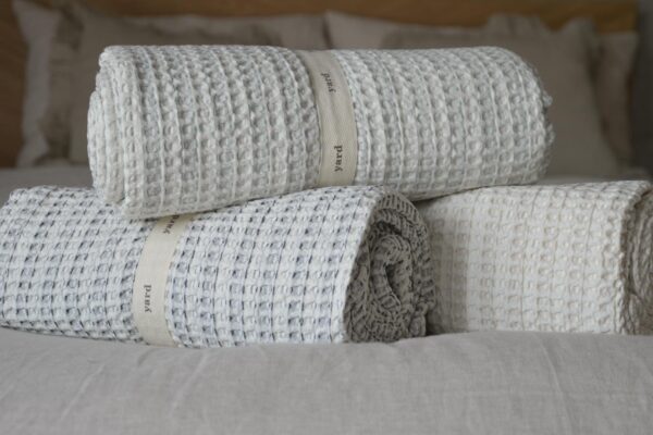 Close up of three rolled up waffle throws. One ivory, one ivory with navy detail, one ivory with green detail.