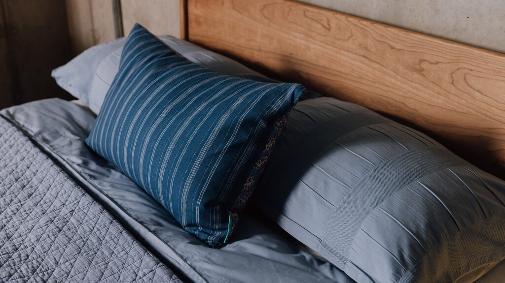 Close up of blue bedding and cushion on a cherry Camden bed.