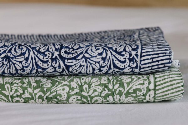 Stack of 2 floral kantha bedspreads folded neatly. Botton green, top blue.