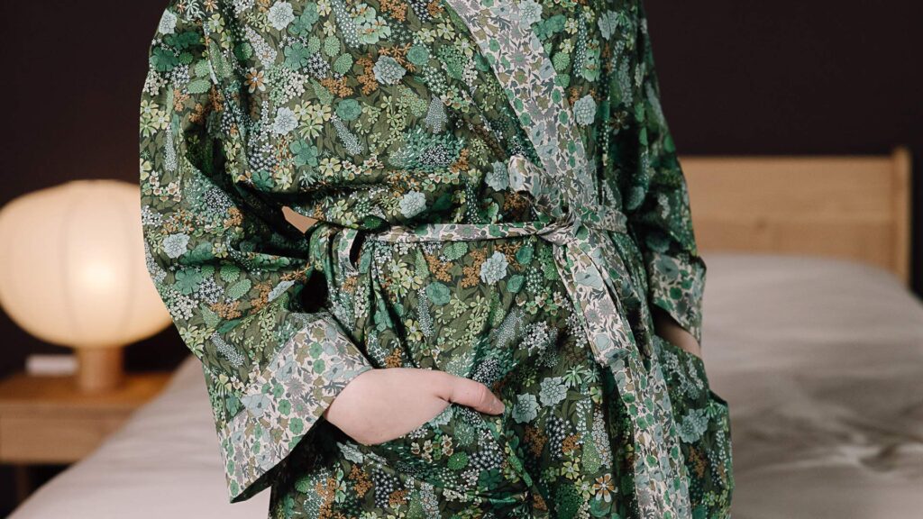 close up Model wearing green floral liberty print robe with hand in pocket.