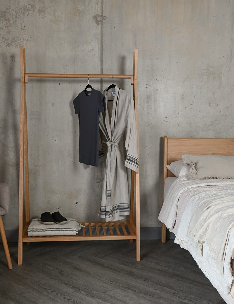 Portrait image showing the Solid Oak Freestanding Clothes Rail with a t-shirt and cotton robe hanging from it.