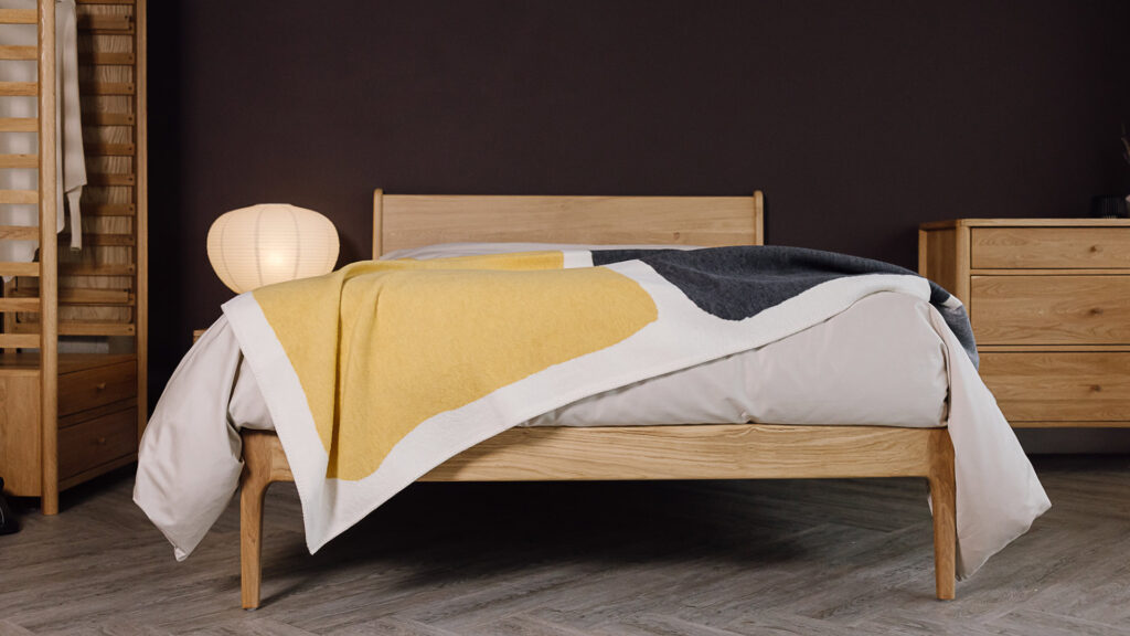 grey and yellow block colour throw draped over neutral duvet cover on an oak bed. Bedroom scene includes other oak furniture.