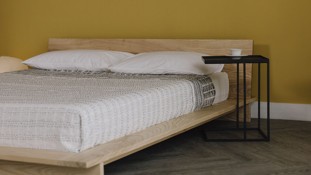 3/4 view of the Oregon bed frame in ash, with a metal side table.