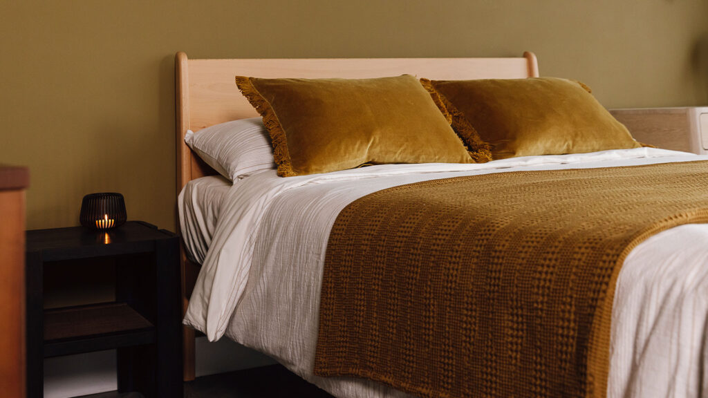 Beech Camden bed with beige and ivory striped bedding and matching mustard gold throw and cushions.