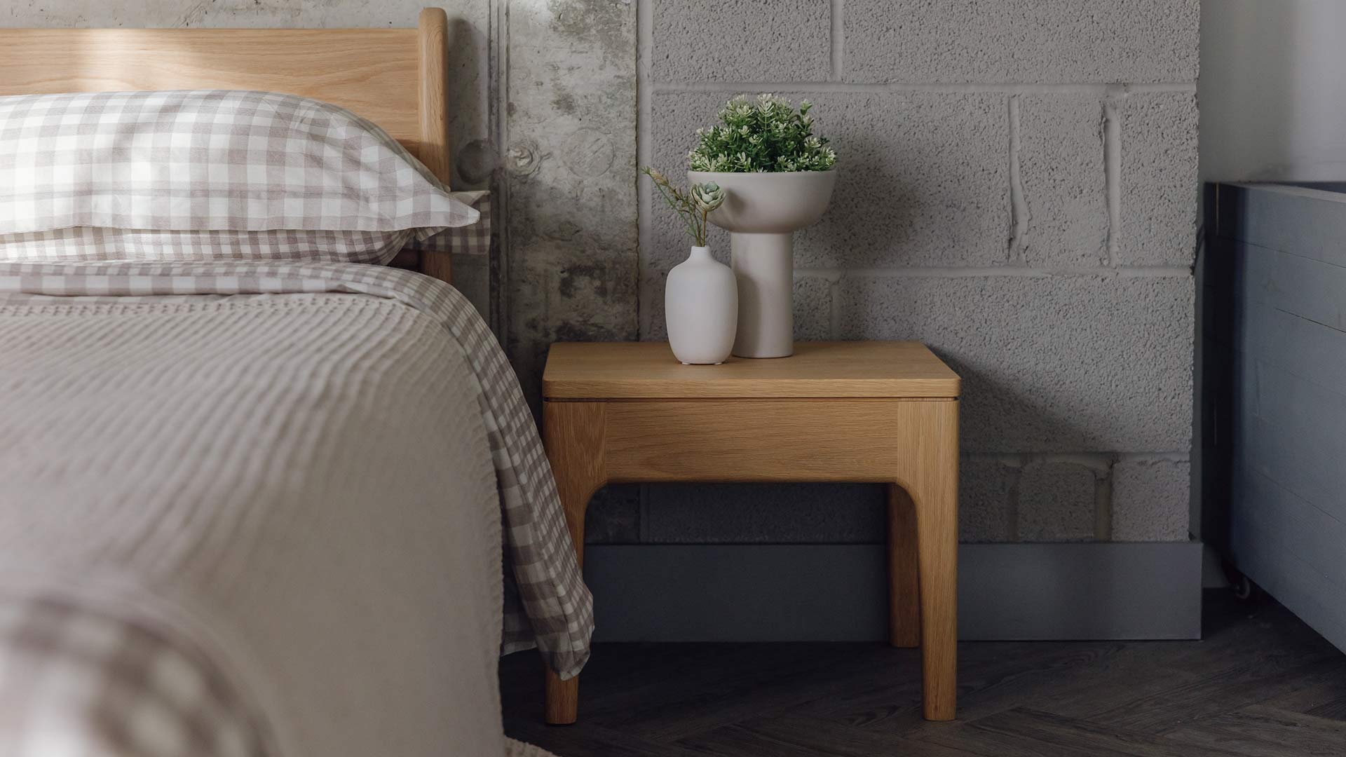 Original Oak Camden table with vases, placed next to an oak Pimlico bed with beige gingham bedding and matching bedspread.