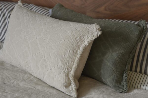 A light ecru textured cushion stacked in front of an olive green textured cushion, showing the fringe details.