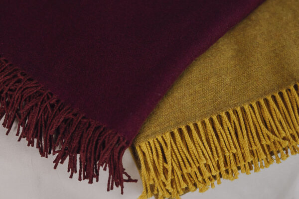 2 Rich merino throws with tassels neatly folded on bed. One mustard yellow, one deep wine.