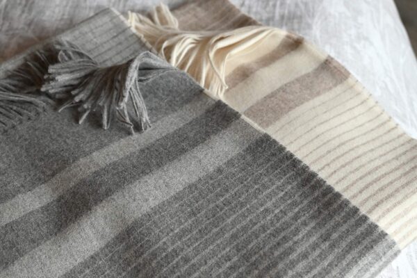 A folded stack of striped woollen throws in the colours Cappuccino and Cool Grey.