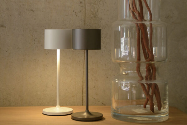 White and burnished metal mini LED lamps stood on table next to large glass vase.