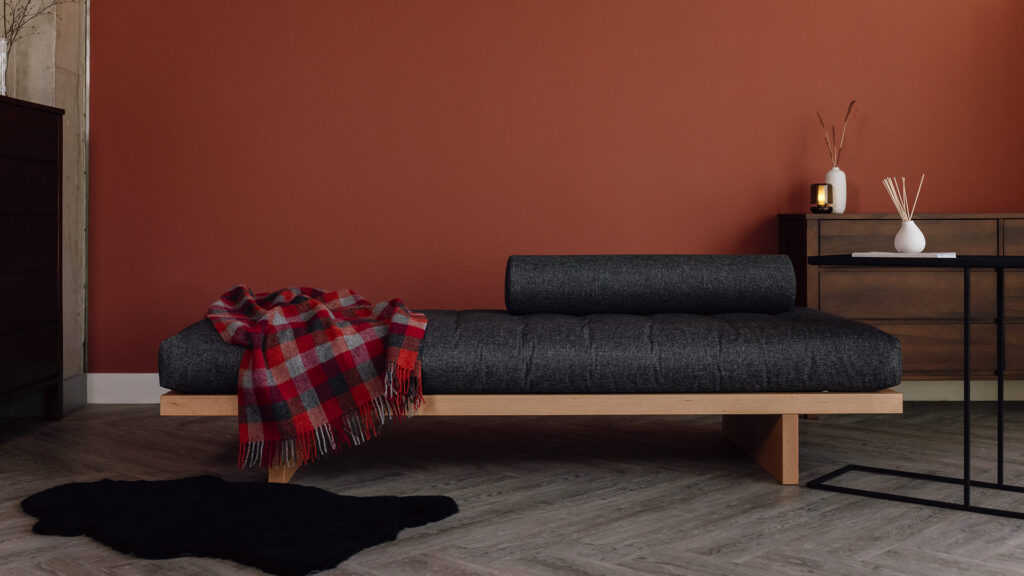 Modern daybed in cherry with a larmony anthracite mattress photographed with a red and grey check blanket across one side.