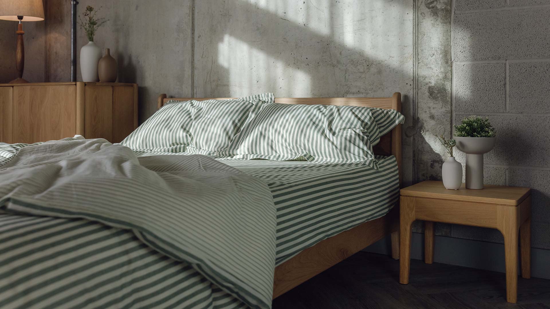 Low oak Pimlico bed base with rumpled green and ivory stripes bedding. Pictured with the original Camden table in oak with vases of greenery.