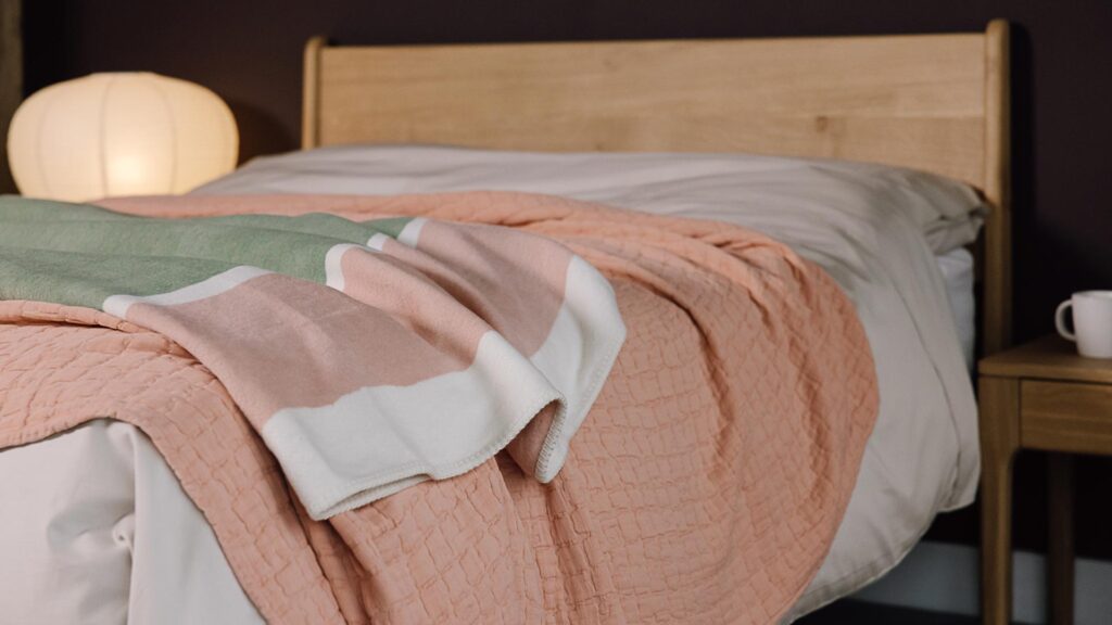 close up of light pink and green throws draped across bed.
