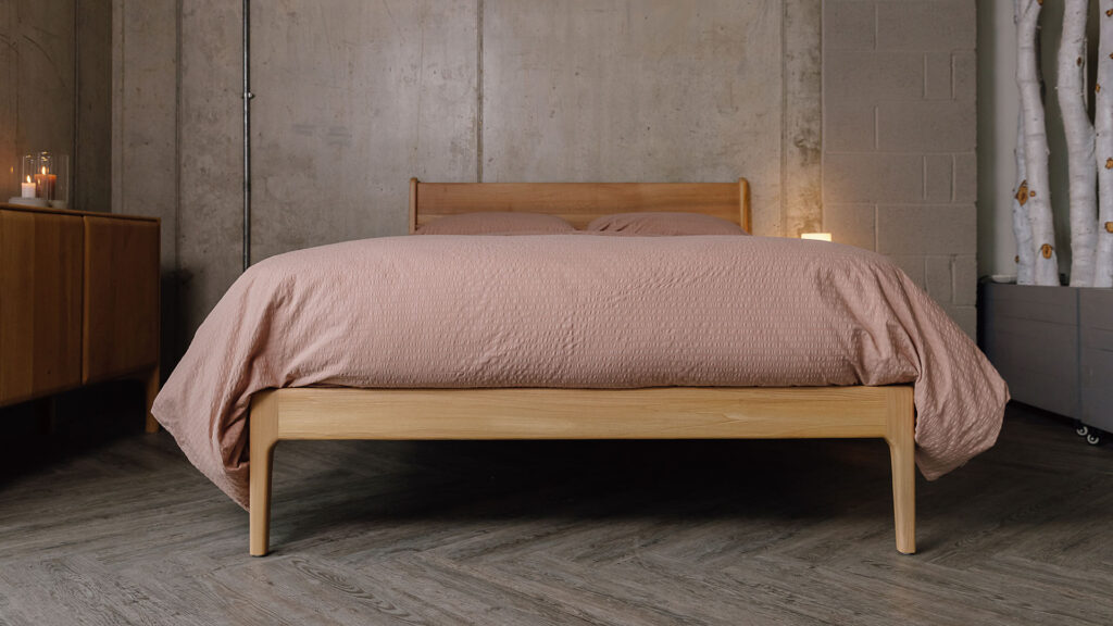 Low down view of Scottish Elm Camden bed with seersucker bedding in dusty pink.