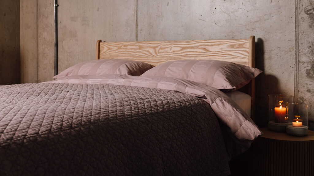 pink textured bedding with pink quilted bedspread on a solid ash bed frame.