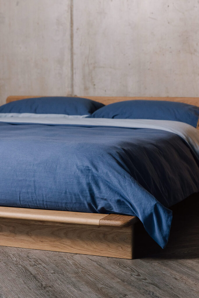 bottom corner of low platform bed dressed in reversible blue linen bedding.