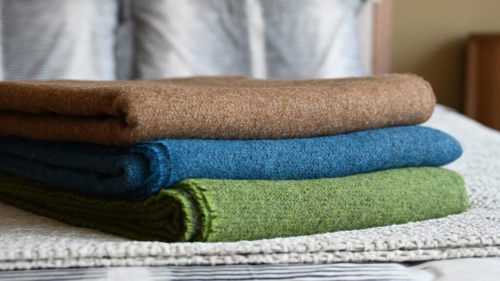Stack of pure wool reversible throws. Front angled view, various colours.