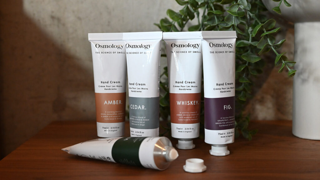 Amber, cedar, whiskey and fig scented hand creams standing in a row. Open tube laying in front.