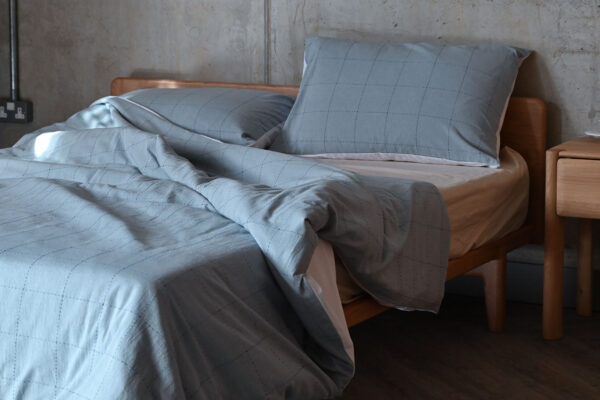 A close shot of a light blue cotton duvet set with dark blue square embroidery, displayed on a solid cherry Osaka bed base.
