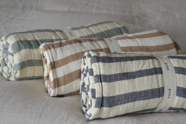 Three throws rolled up. One with a navy stripe, one rust and one green.