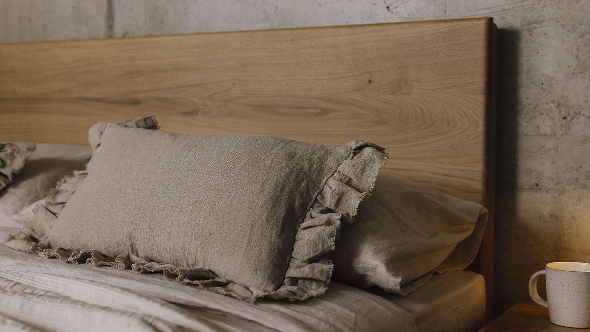 close up of ruffled edge linen cushion on bed with oak headboard.